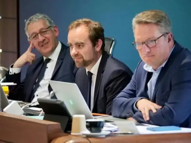 Trois hommes en costume à une table de réunion