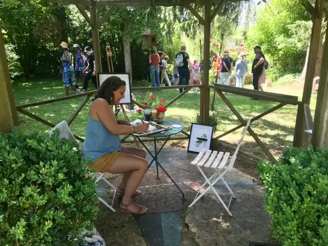 Fête de la Peinture : une peintre à son chevalet dans le jardin, les visiteurs en arrière-plan
