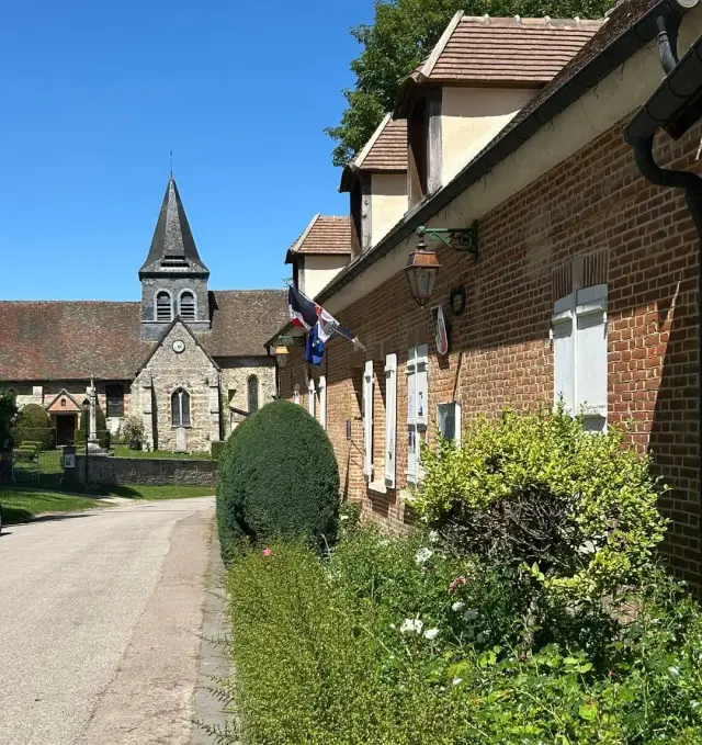 La rue de la mairie : la façade en brique et ses drapeaux, l’église en arrière-plan